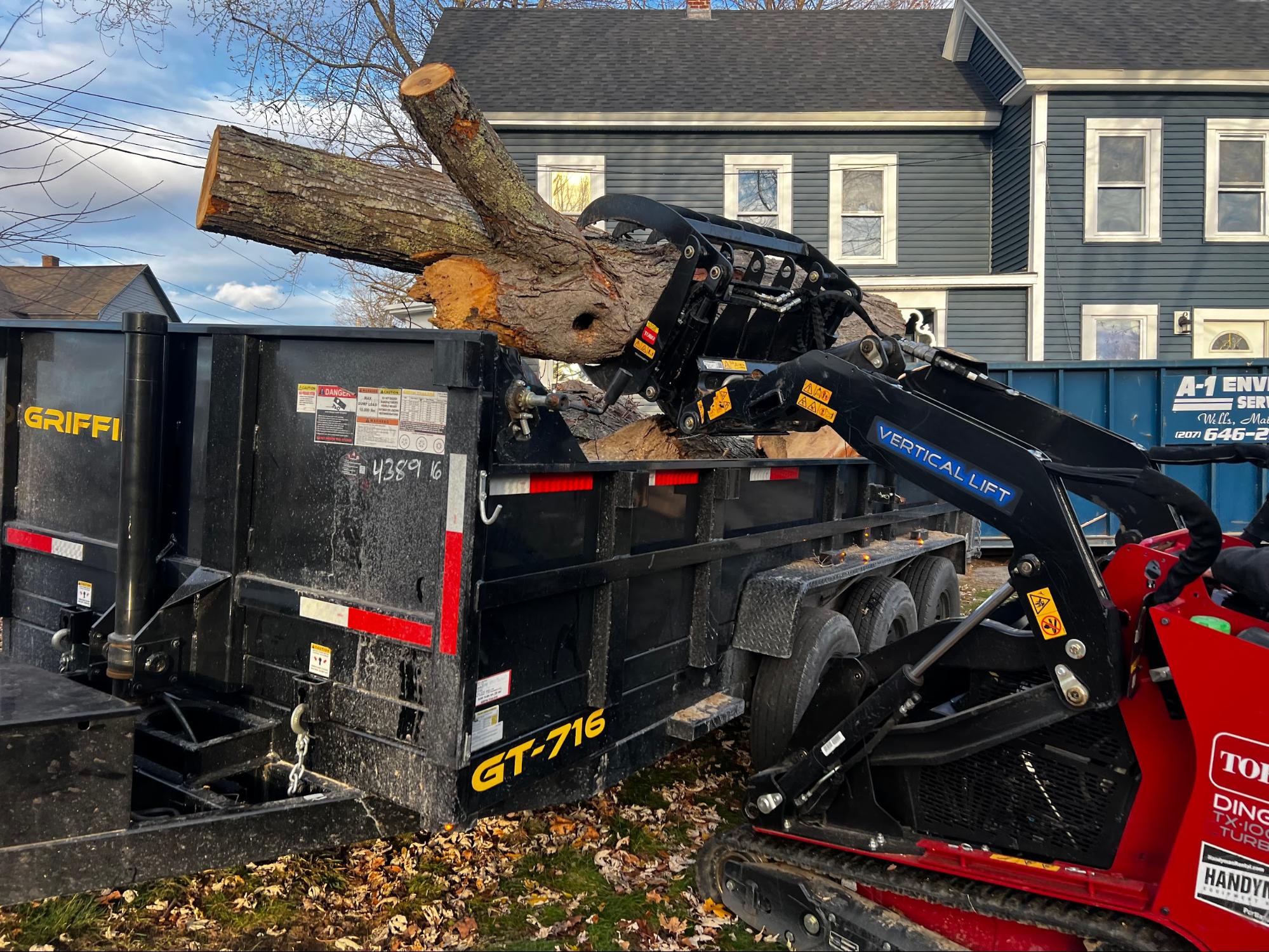 Skid steer lifting large log into trailer
